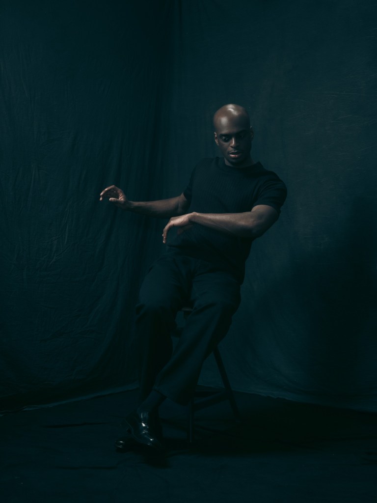 Fine art portrait of Kioff by De Sheng Lim, a portrait photographer based in The Hague, Netherlands. Kioff is captured mid-movement while seated, creating a dynamic silhouette against a textured dark background.
